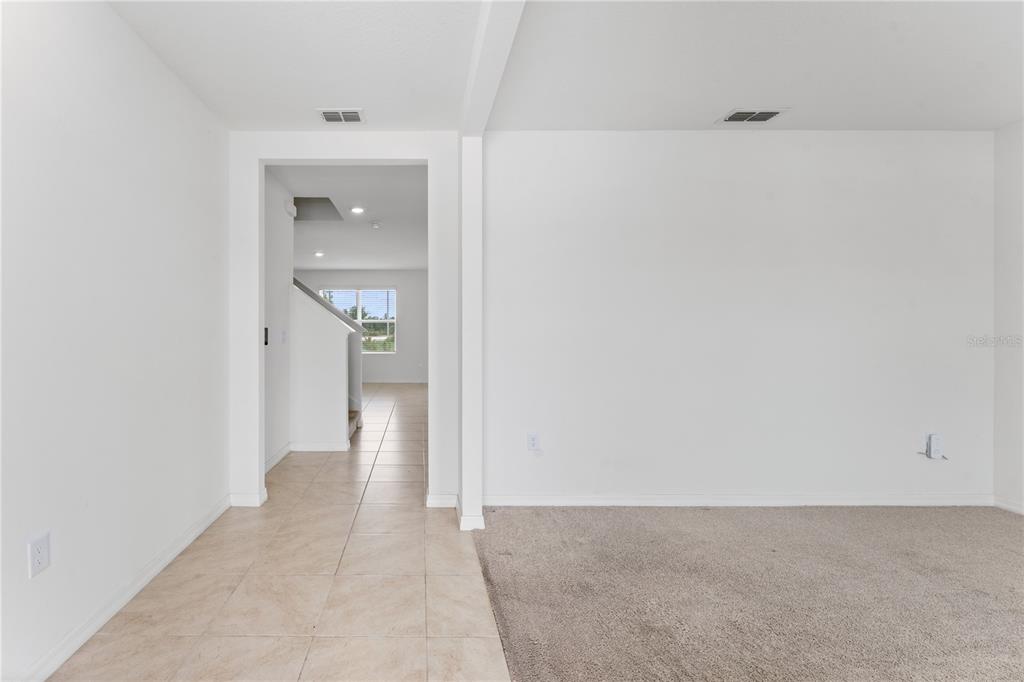 A room with beige carpet transitions to a tiled hallway leading to a staircase — 5038 FOXGLOVE CIRCLE, LAKELAND, FL