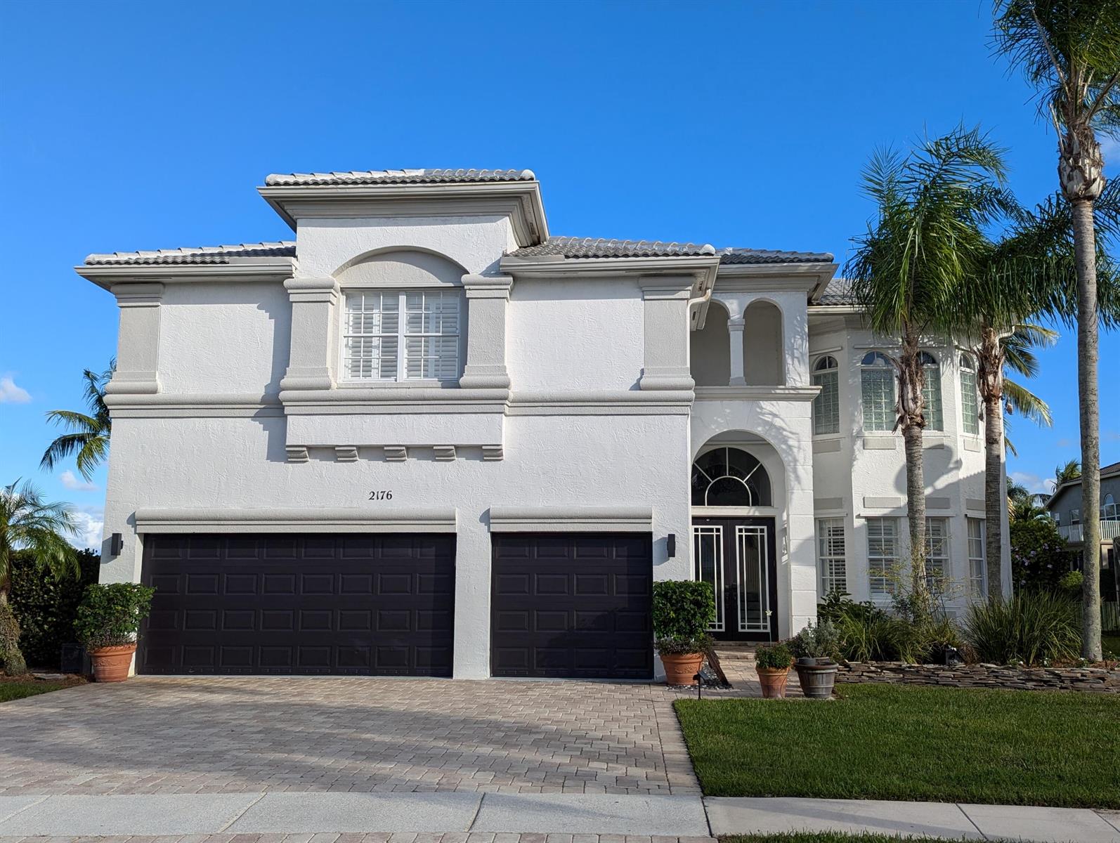 A two-story white stucco house features a three-car garage and a prominent arched entryway — 2176 Bellcrest Circle, Royal Palm Beach FL 33411, ROYAL PALM BEACH, FL