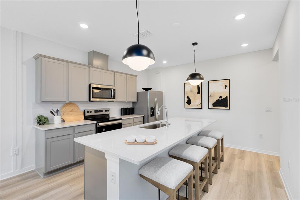 A modern kitchen features gray cabinets, a white quartz island with bar stools, and pendant lighting — 6262 SUNNY TIME AVENUE, WINTER GARDEN, FL
