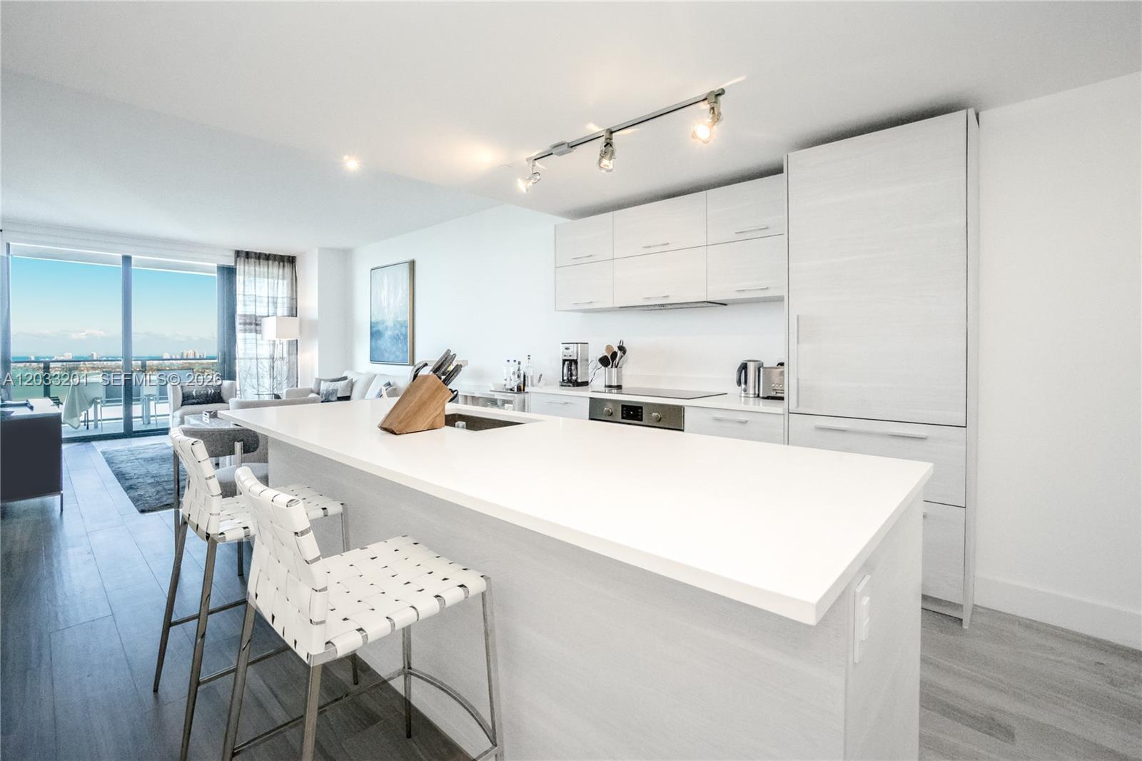 A modern kitchen features white cabinetry, a large island with bar seating, and balcony views — 650 NE 32nd St # 3505, Miami FL 33137, MIAMI, FL