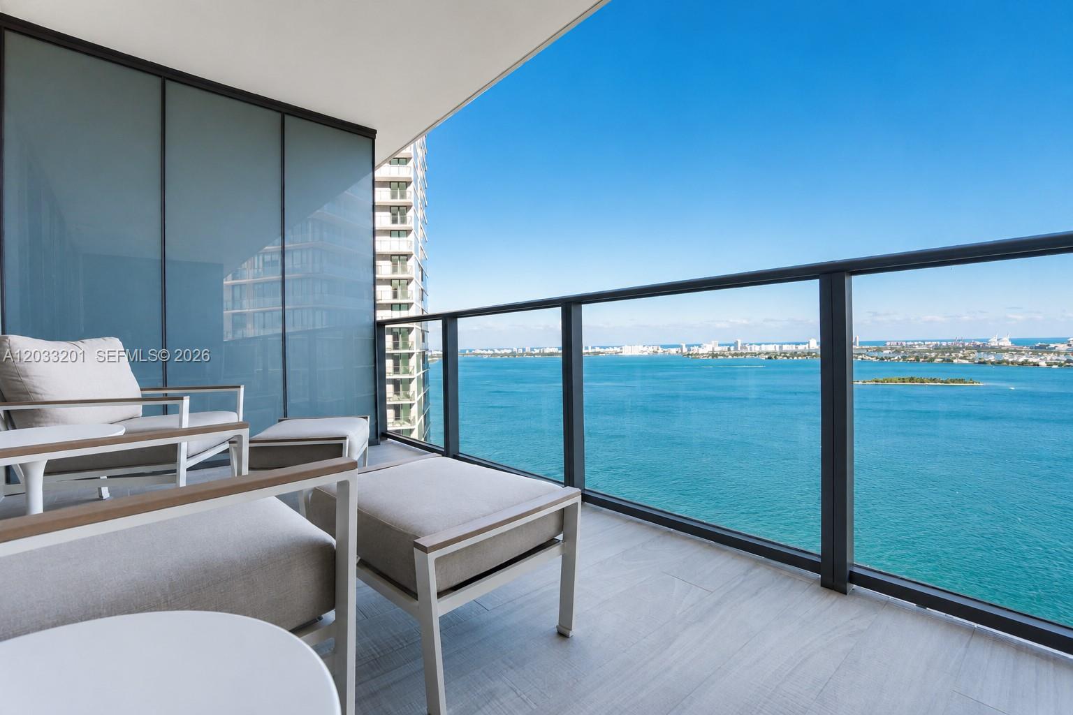 A balcony with outdoor seating overlooks a bay and city skyline under a clear sky — 650 NE 32nd St # 3505, Miami FL 33137, MIAMI, FL