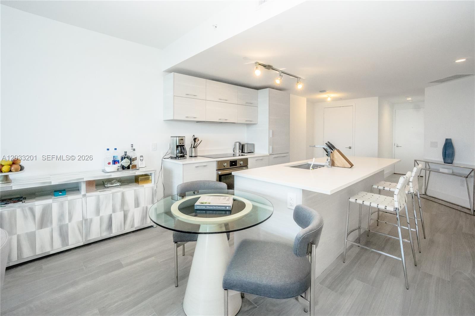 A modern kitchen features white cabinetry, a central island with bar seating, and a dining area — 650 NE 32nd St # 3505, Miami FL 33137, MIAMI, FL
