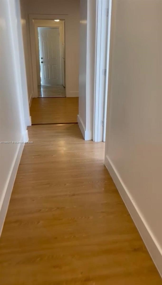 A hallway with light wood-look flooring leads to a doorway in a white interior — 506 18th St # B, West Palm Beach FL 33407, WEST PALM BEACH, FL