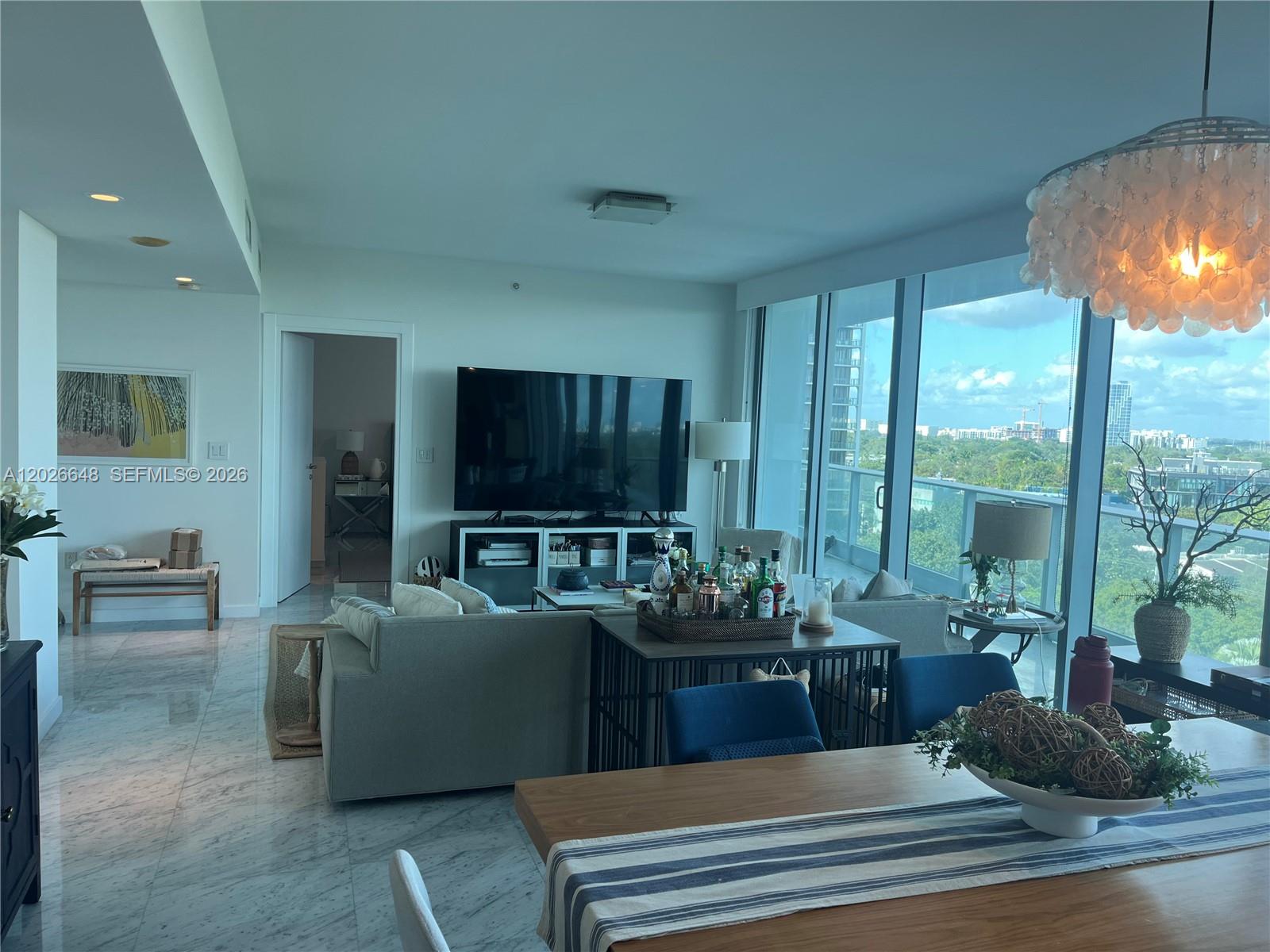 A modern living and dining area features marble floors, floor-to-ceiling windows, and a shell chandelier — 2627 S Bayshore Dr # 1208, Miami FL 33133, MIAMI, FL