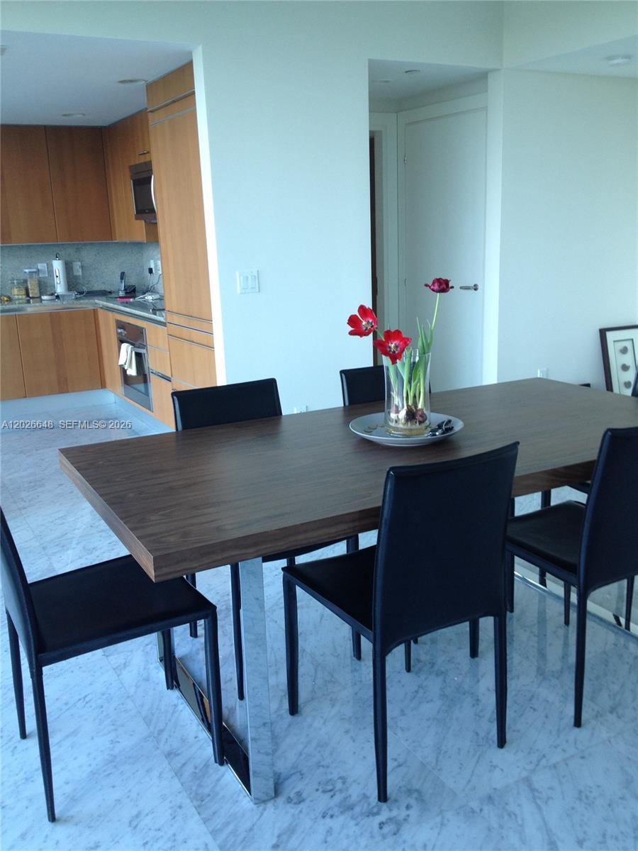 A dining area with a wooden table, black chairs, and an adjacent kitchen — 2627 S Bayshore Dr # 1208, Miami FL 33133, MIAMI, FL