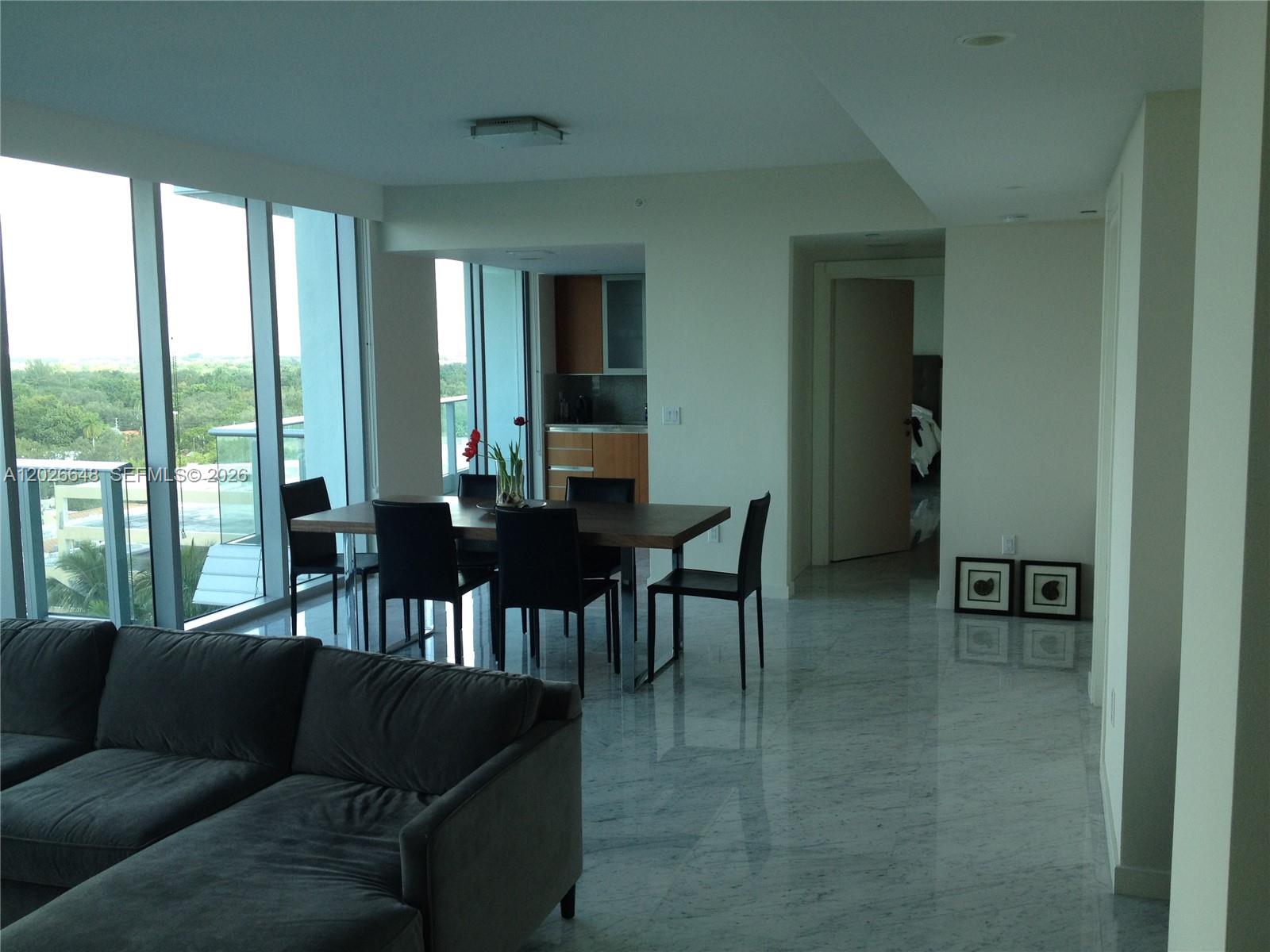A modern dining area with a wooden table and chairs sits beside floor-to-ceiling windows — 2627 S Bayshore Dr # 1208, Miami FL 33133, MIAMI, FL