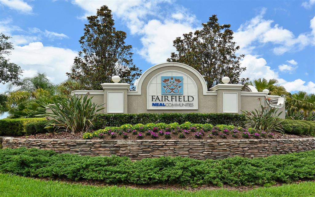 A stone-walled entrance sign for Fairfield by Neal Communities sits amidst landscaped greenery and trees — 4956 MAYMONT PARK CIRCLE, BRADENTON, FL