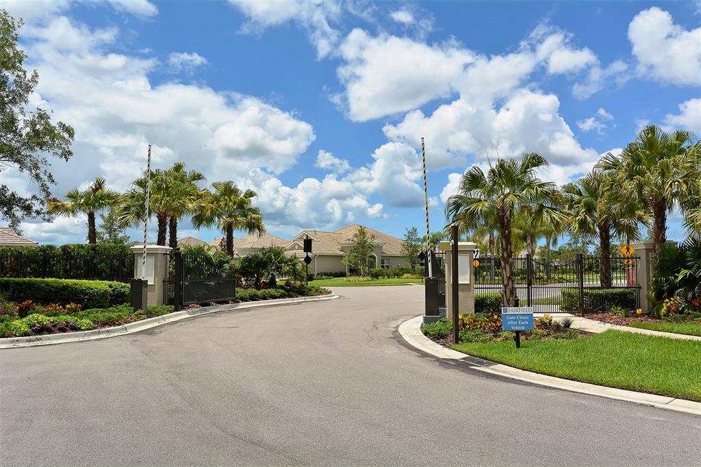 A gated entrance with palm trees and a paved road leading to residential homes — 4956 MAYMONT PARK CIRCLE, BRADENTON, FL