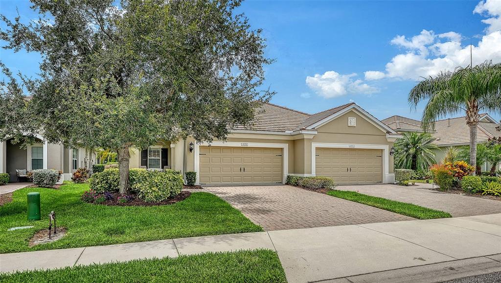 A tan single-story house with a three-car garage and a large tree in the yard — 4956 MAYMONT PARK CIRCLE, BRADENTON, FL