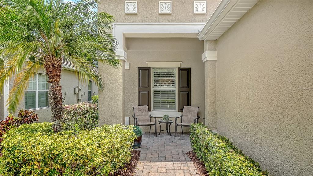 A paved entryway features two chairs, a small table, and a window with dark shutters — 4956 MAYMONT PARK CIRCLE, BRADENTON, FL