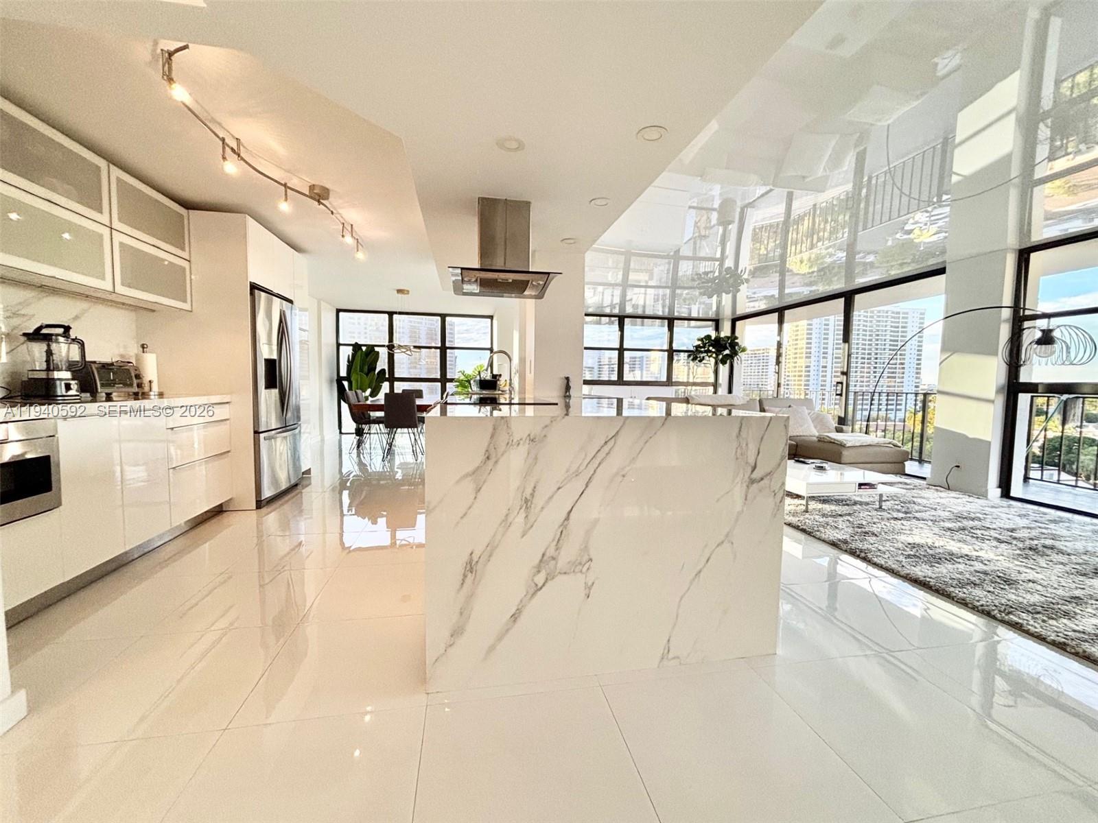 A modern kitchen features a marble waterfall island, white cabinetry, and floor-to-ceiling windows — 200 Leslie Dr # 831, Hallandale Beach FL 33009, HALLANDALE BEACH, FL