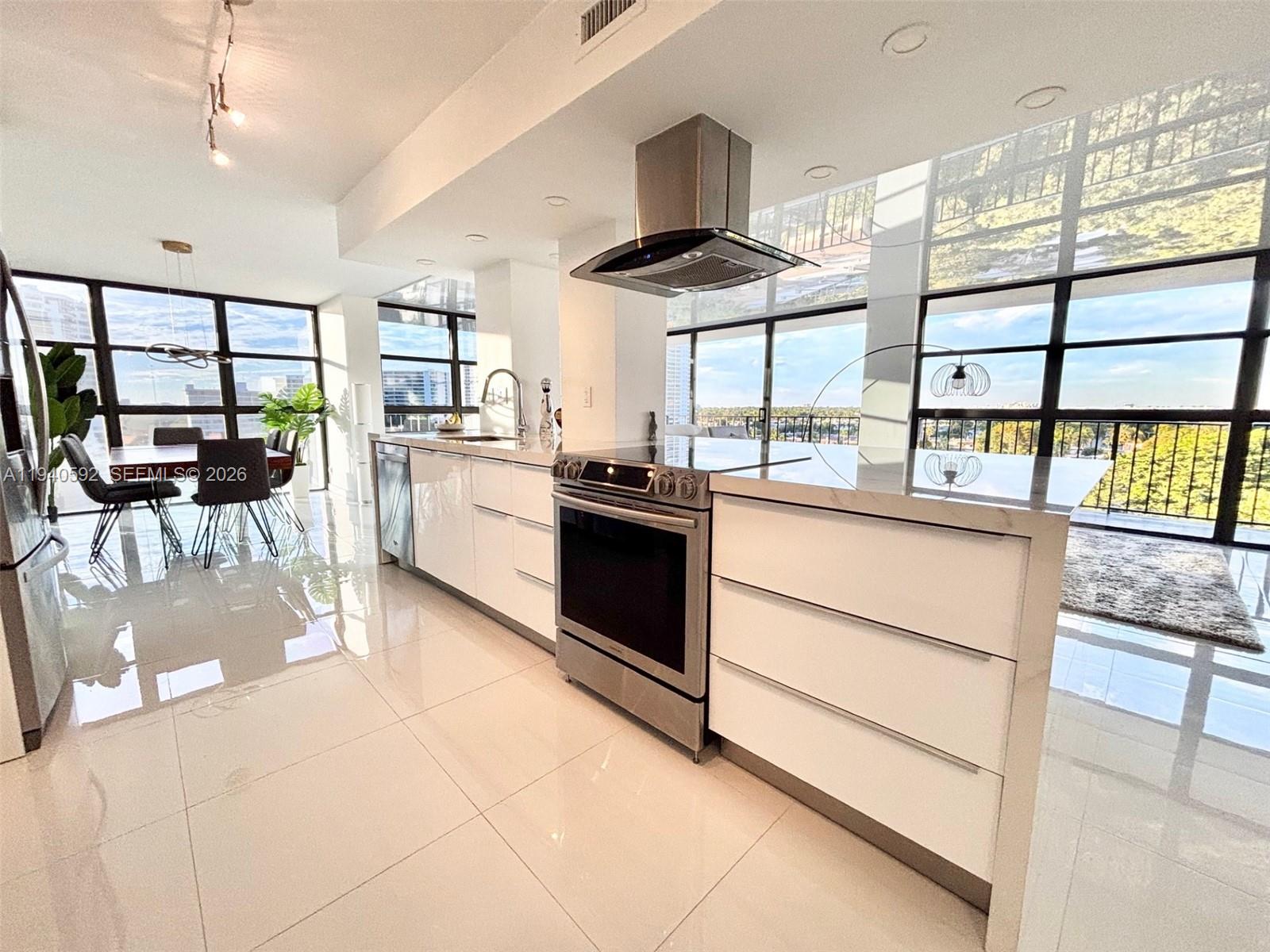 A modern kitchen features white cabinetry, stainless steel appliances, and floor-to-ceiling windows with city views — 200 Leslie Dr # 831, Hallandale Beach FL 33009, HALLANDALE BEACH, FL
