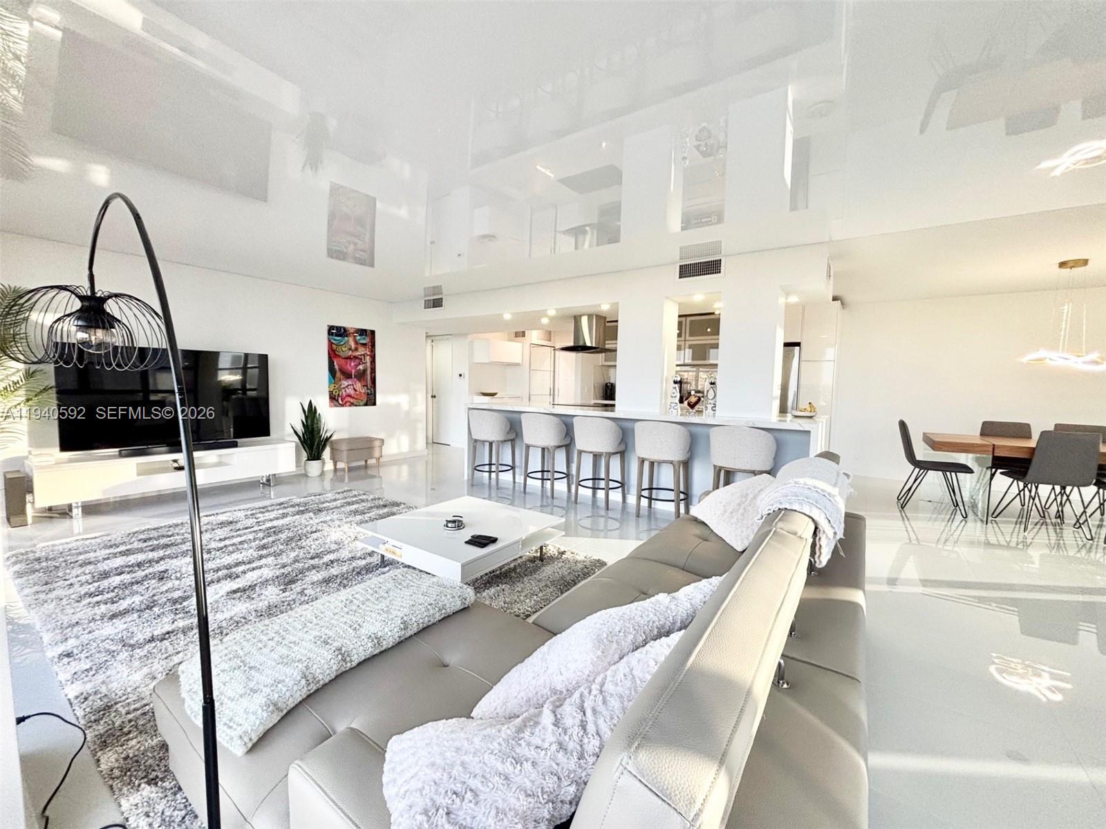 A modern open-concept living room features a glossy white ceiling, tiled floors, and kitchen bar — 200 Leslie Dr # 831, Hallandale Beach FL 33009, HALLANDALE BEACH, FL