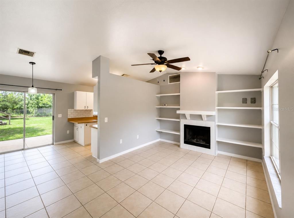 A living room with tile flooring, a fireplace, built-in shelving, and an adjacent kitchen area — 6108 PECAN COURSE, OCALA, FL