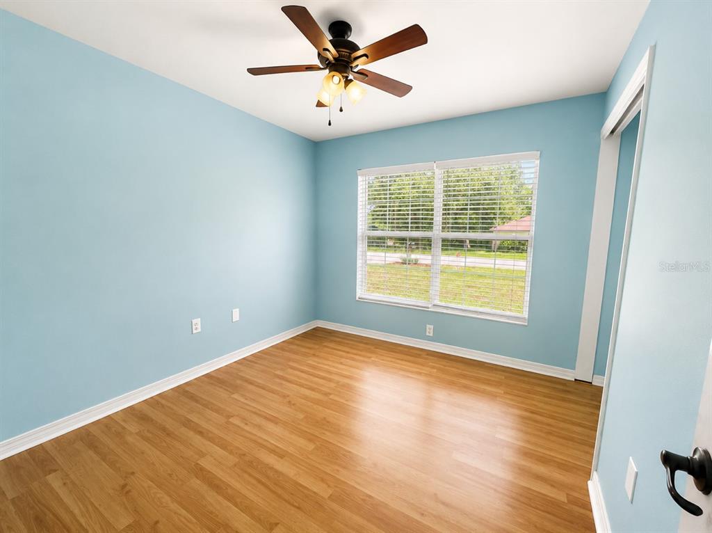 An empty bedroom with light blue walls, wood-look flooring, a ceiling fan, and a window — 6108 PECAN COURSE, OCALA, FL