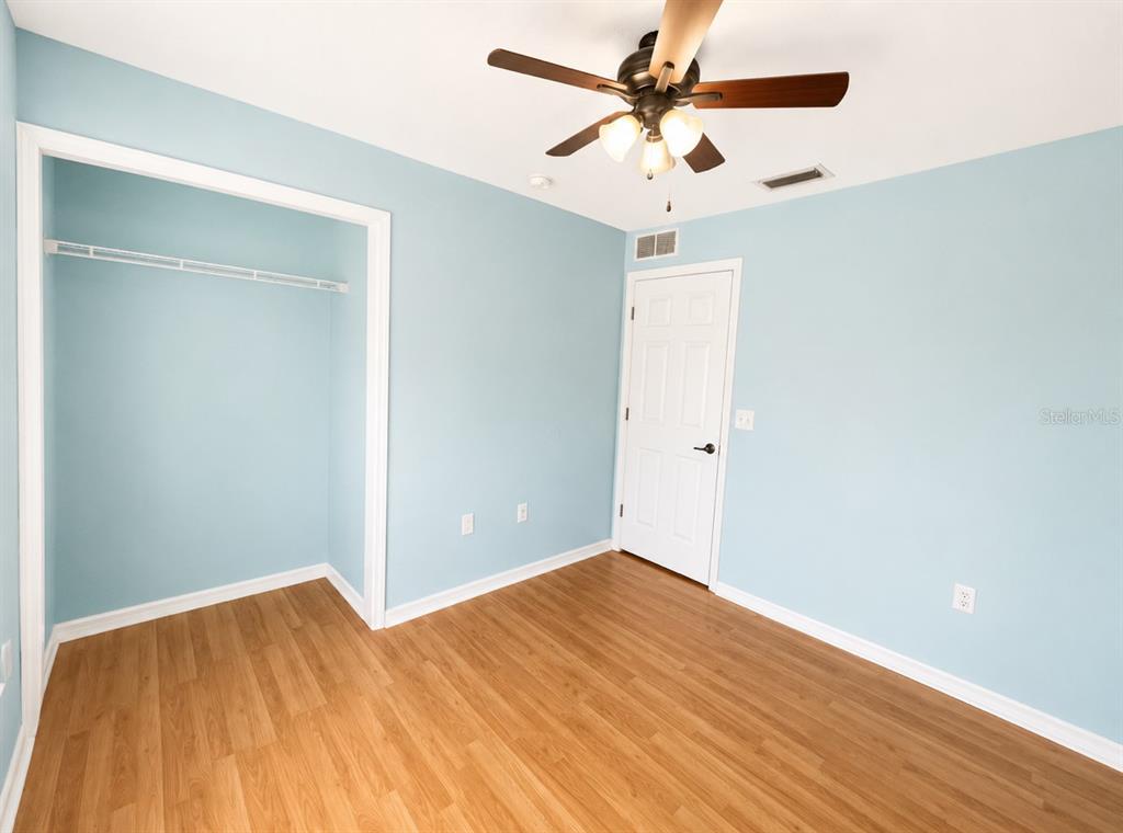 A bedroom with light blue walls, wood-look flooring, a ceiling fan, and a closet — 6108 PECAN COURSE, OCALA, FL