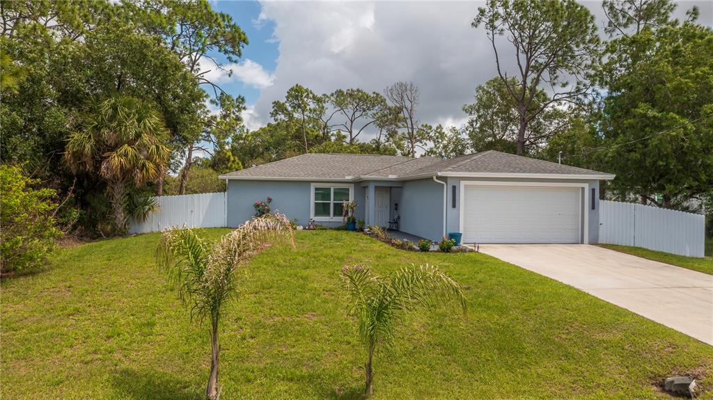 A single-story blue house with a white garage door and a fenced front yard — 7081 BRAZIL CIRCLE, LABELLE, FL