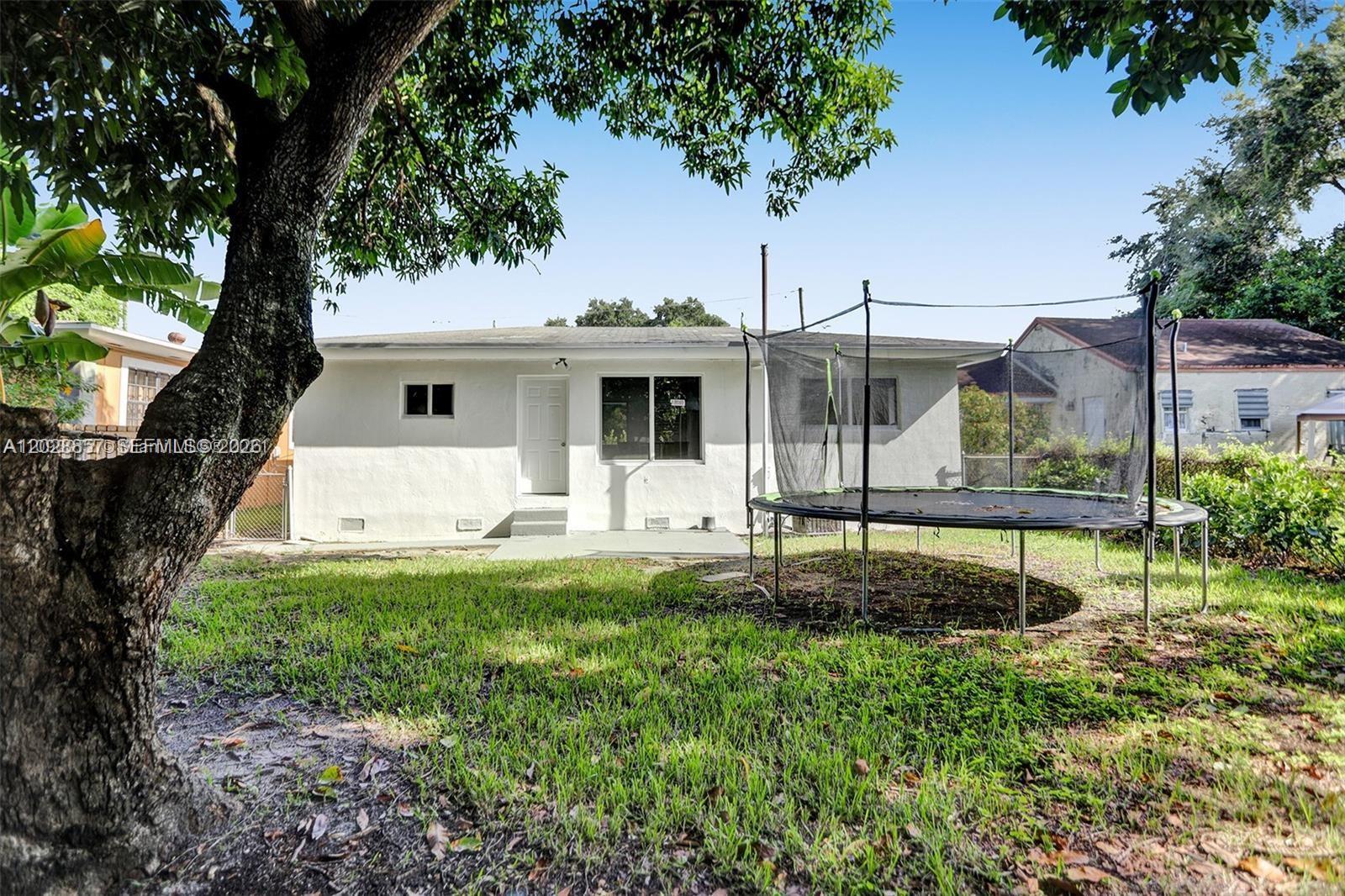 The exterior of a white house features a backyard with a trampoline and a large tree — 236 NW 42nd St, Miami FL 33127, MIAMI, FL