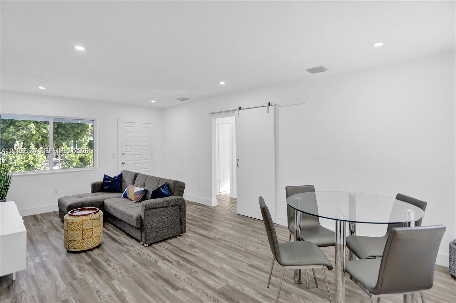 A living and dining area features gray wood-look flooring, white walls, and a sliding barn door — 236 NW 42nd St, Miami FL 33127, MIAMI, FL
