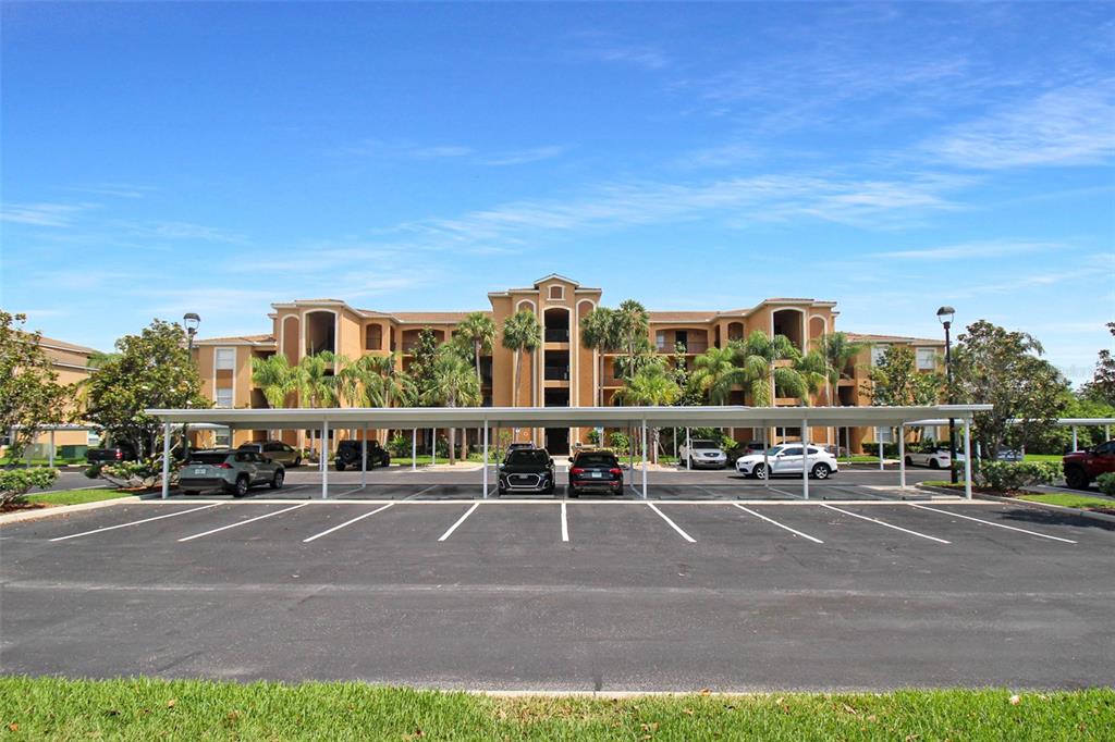 A multi-story apartment building with a covered parking structure in the foreground — 8403 GRAND ESTUARY TRAIL UNIT 205, BRADENTON, FL