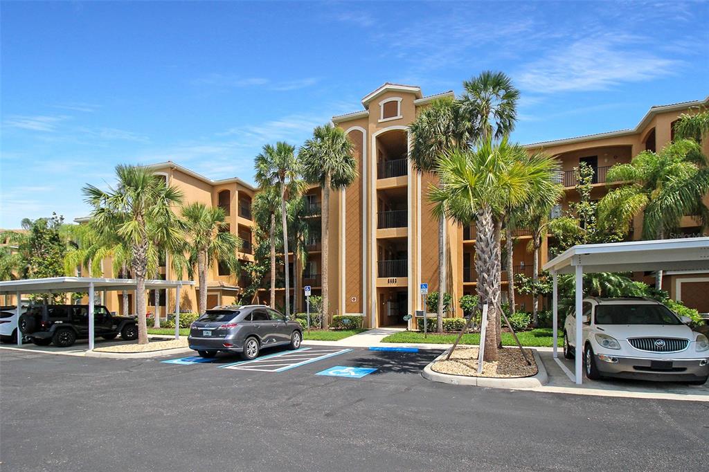 A multi-story apartment building with a parking lot and palm trees in the foreground — 8403 GRAND ESTUARY TRAIL UNIT 205, BRADENTON, FL