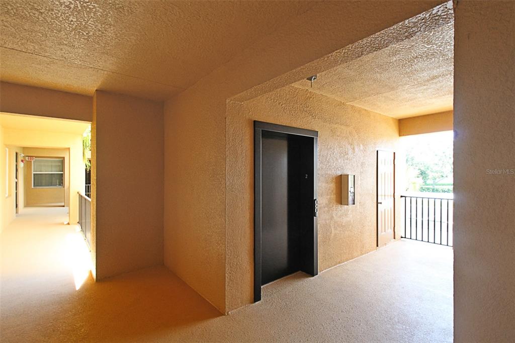 An outdoor apartment hallway features a black elevator door, a utility door, and textured walls — 8403 GRAND ESTUARY TRAIL UNIT 205, BRADENTON, FL