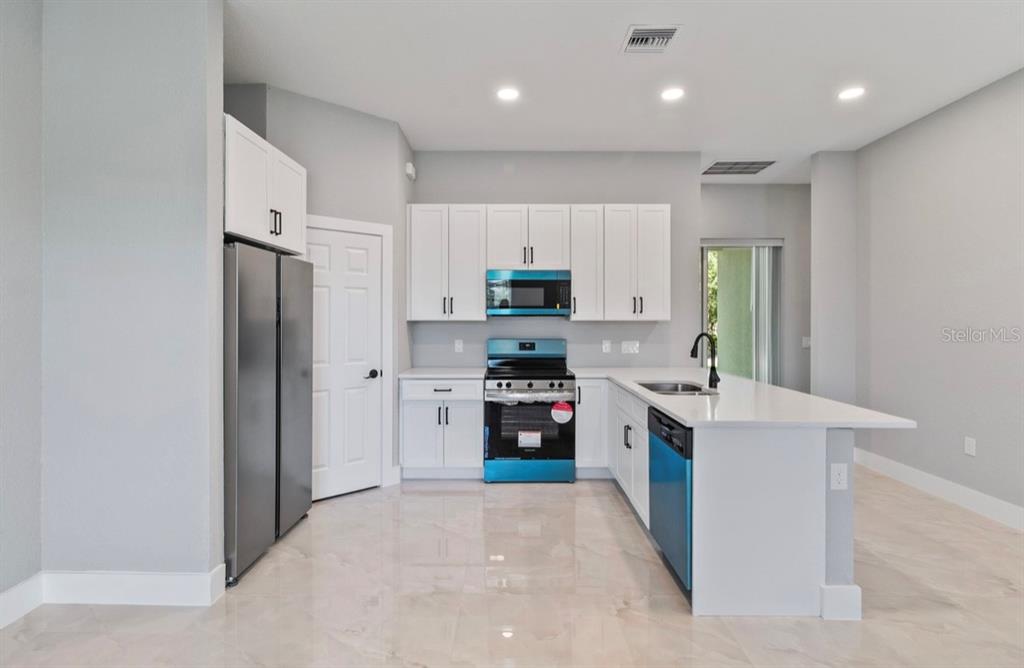 A kitchen features white cabinets, stainless steel appliances, a kitchen island, and light tile flooring — 20462 KENILWORTH BOULEVARD, PORT CHARLOTTE, FL