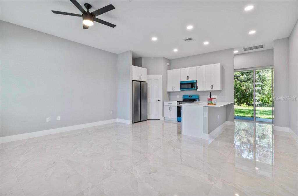 A modern kitchen and living area with white cabinets, stainless appliances, and light tile flooring — 20462 KENILWORTH BOULEVARD, PORT CHARLOTTE, FL