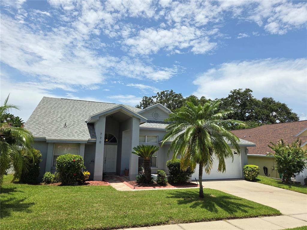 A single-story gray house with a palm tree, a two-car garage, and a landscaped lawn — 770 WILDFLOWER DRIVE, PALM HARBOR, FL