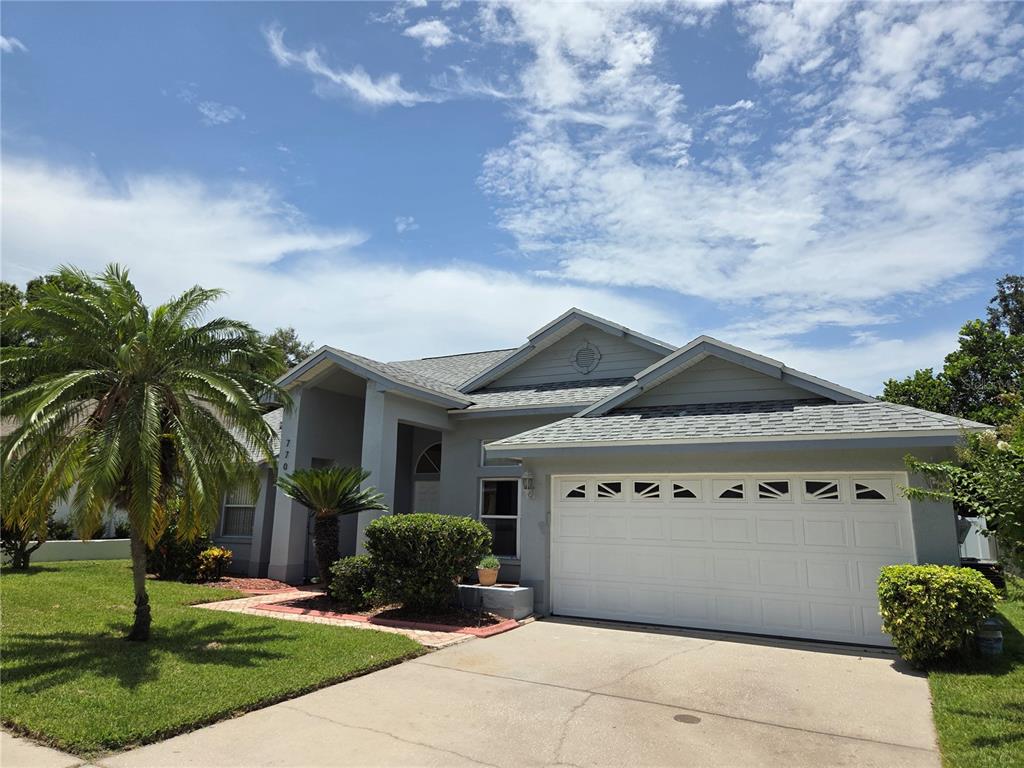 A single-story house with a gray exterior, a two-car garage, and a palm tree — 770 WILDFLOWER DRIVE, PALM HARBOR, FL