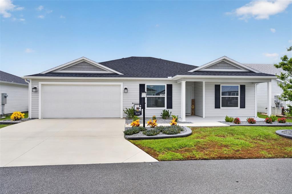 A single-story house with light gray siding, a two-car garage, and a covered front porch — 7686 WOODLEY TERRACE, THE VILLAGES, FL