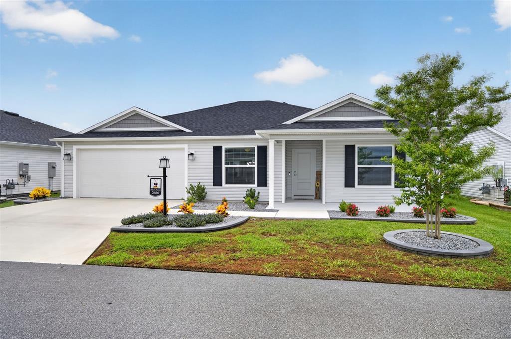 A single-story house with light gray siding, a two-car garage, and a landscaped front yard — 7686 WOODLEY TERRACE, THE VILLAGES, FL