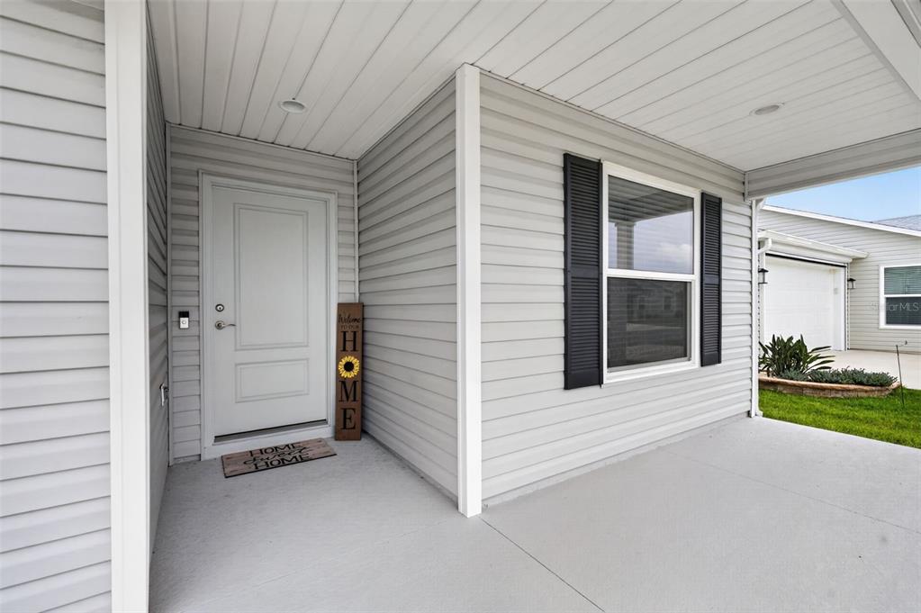 A covered front porch features light gray siding, a white door, and black window shutters — 7686 WOODLEY TERRACE, THE VILLAGES, FL