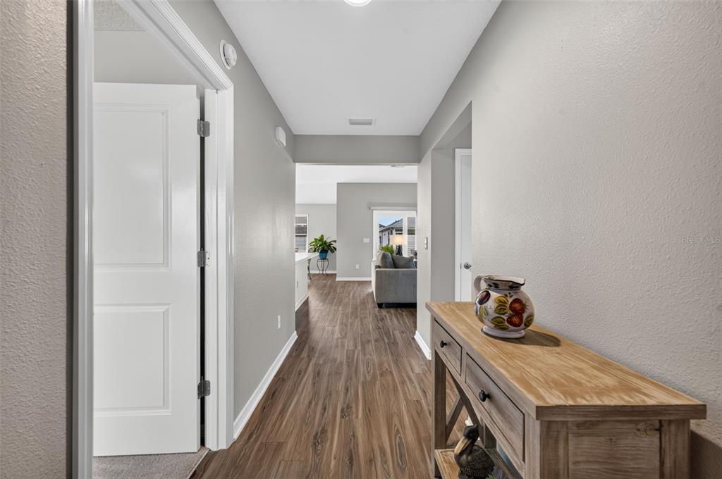 A hallway with wood-look flooring leads from a foreground entryway toward a living area — 7686 WOODLEY TERRACE, THE VILLAGES, FL