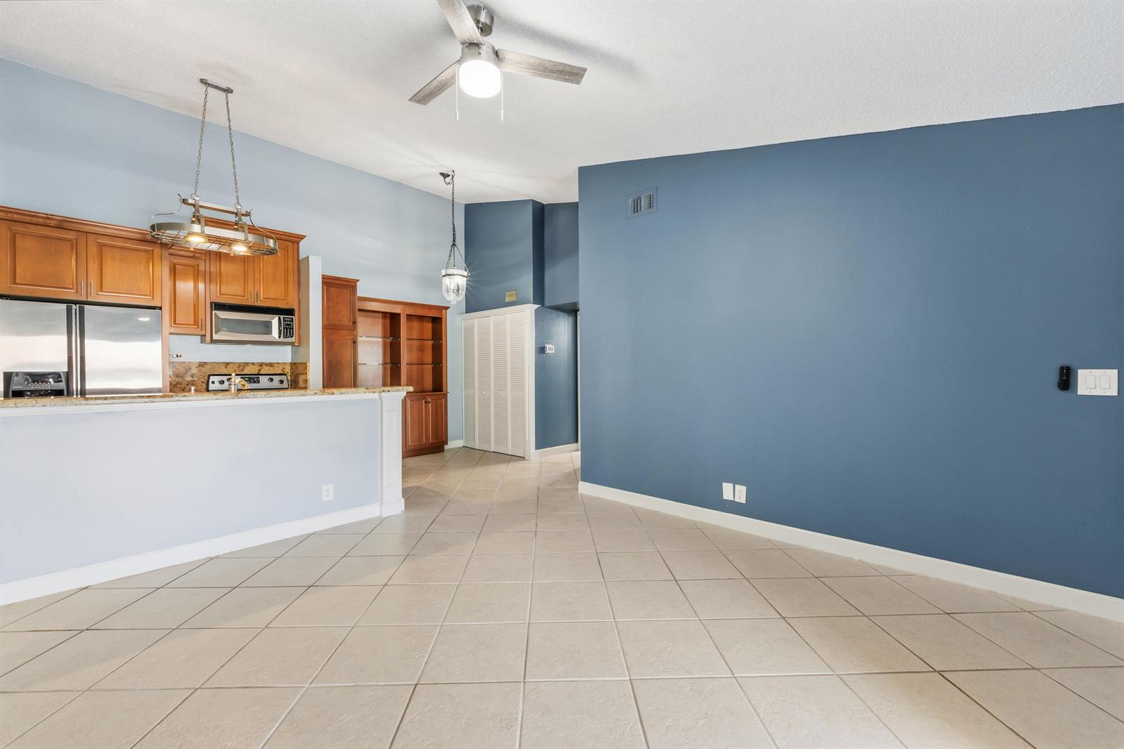 An open-concept room features a kitchen with wood cabinets, tile flooring, and blue walls — 6314 Chasewood Drive, Jupiter FL 33458, JUPITER, FL