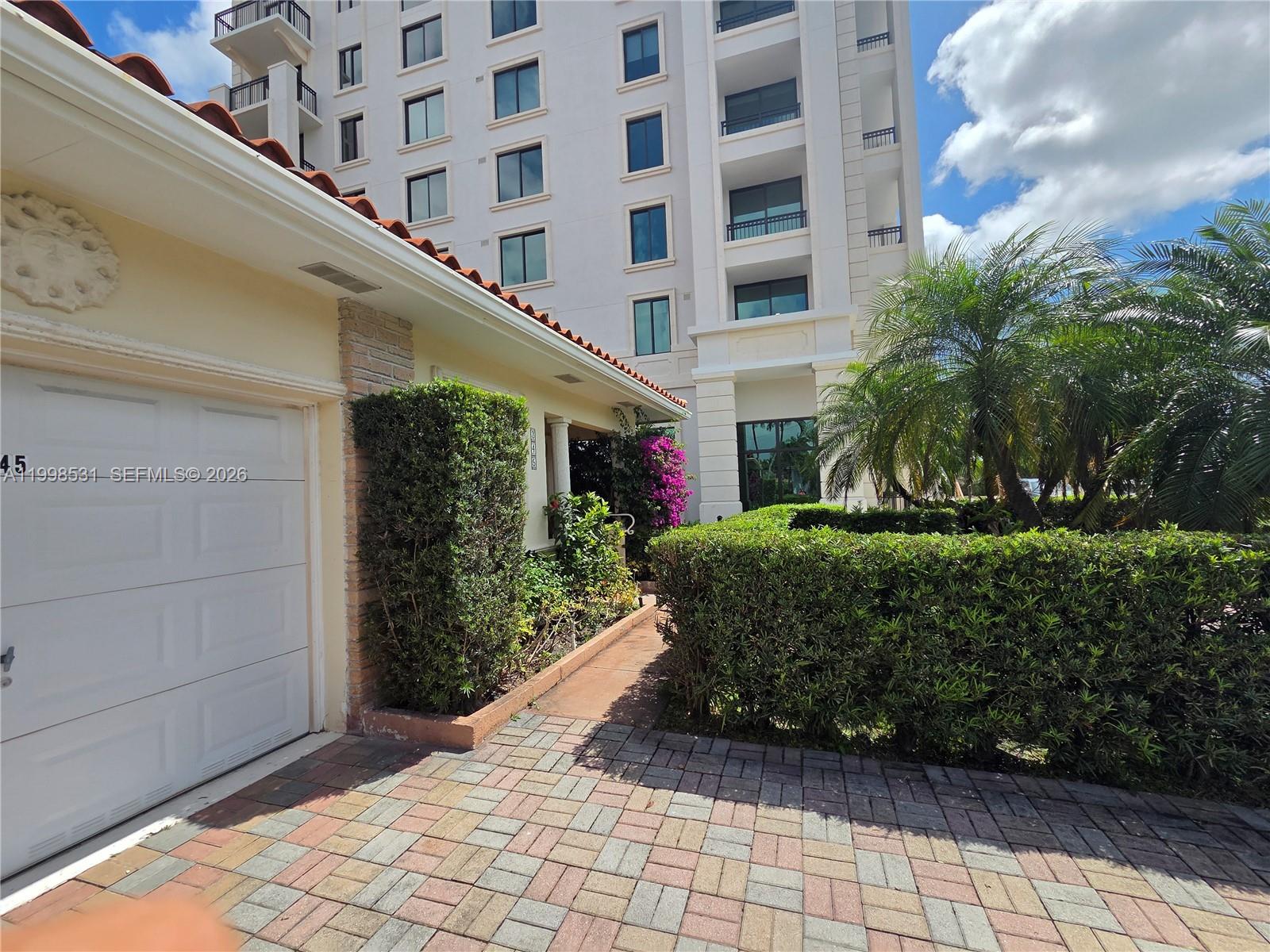 A paved driveway leads to a garage and a walkway beside a tall residential building — 345 Malaga Ave, Coral Gables FL 33134, CORAL GABLES, FL