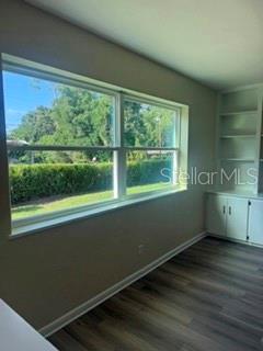A room with wood-look flooring, a large window overlooking trees, and built-in white shelving — 3115 SE 11TH STREET, OCALA, FL