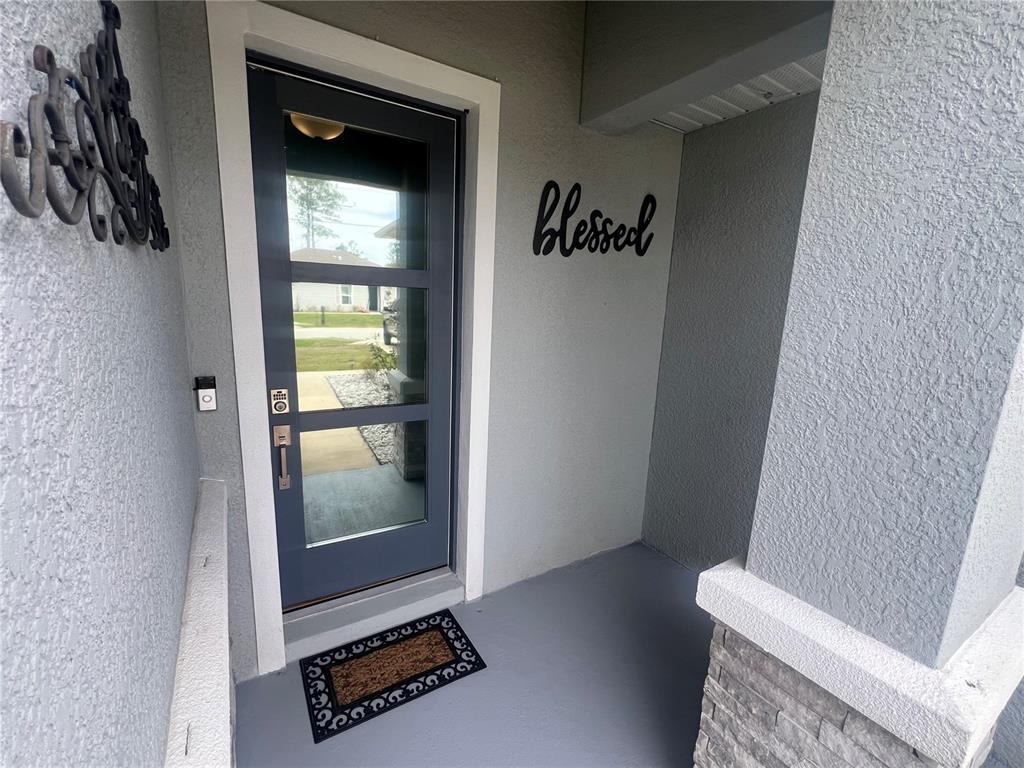 A gray front door with glass panels sits under a covered entryway with a doormat — 41 WHITE STAR DRIVE, PALM COAST, FL