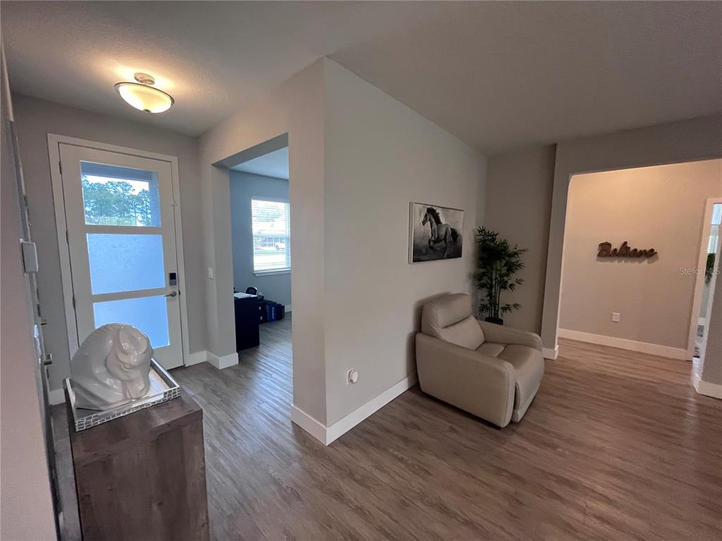 An entryway with light wood flooring, a glass-paneled door, a beige armchair, and wall art — 41 WHITE STAR DRIVE, PALM COAST, FL