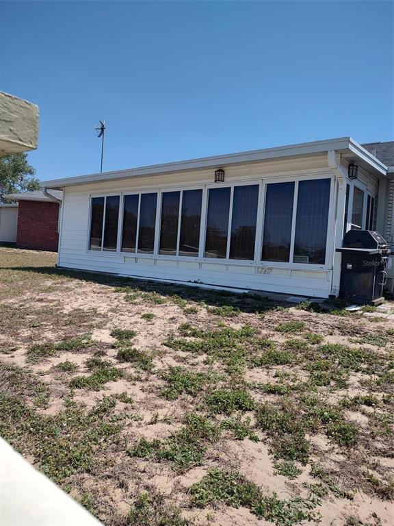 A white exterior sunroom with large windows sits on a sandy lot with sparse vegetation — 1402 THOUSAND ROSES DR. W. UNIT 1402, LAKE WALES, FL