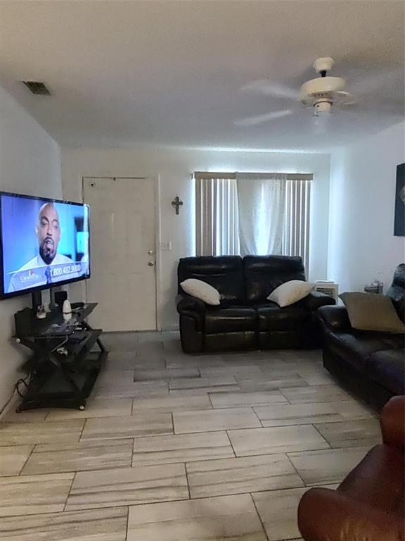 A living room features tiled floors, a ceiling fan, a television, and dark leather furniture — 1402 THOUSAND ROSES DR. W. UNIT 1402, LAKE WALES, FL