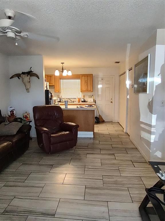 A living room with tile floors and a recliner faces an open kitchen with wood cabinets — 1402 THOUSAND ROSES DR. W. UNIT 1402, LAKE WALES, FL