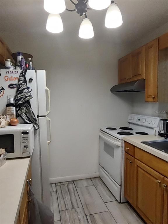 A kitchen features light wood cabinets, white appliances, and gray wood-look tile flooring — 1402 THOUSAND ROSES DR. W. UNIT 1402, LAKE WALES, FL