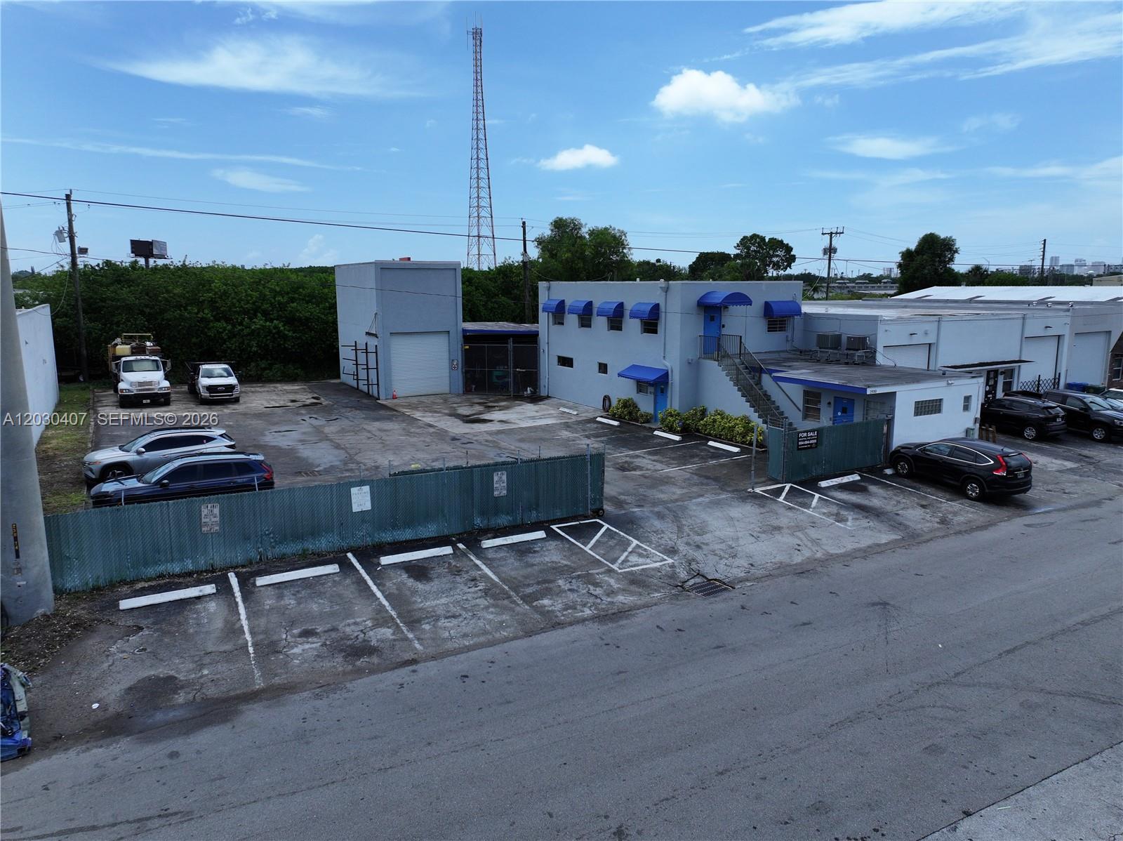 An aerial view shows a light blue commercial building with a fenced parking lot — OAKLAND PARK, FL
