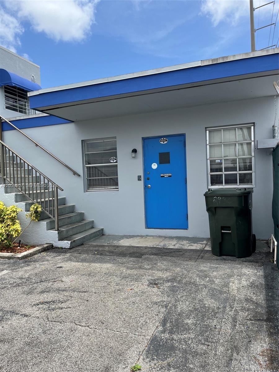 A blue door with a delivery sign sits beside a staircase and a trash bin — OAKLAND PARK, FL