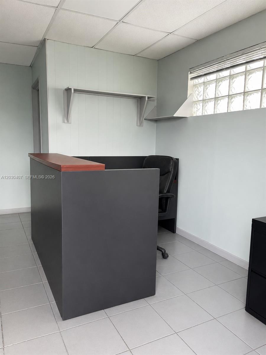 A small office space features a dark reception desk, tile flooring, and a glass block window — OAKLAND PARK, FL
