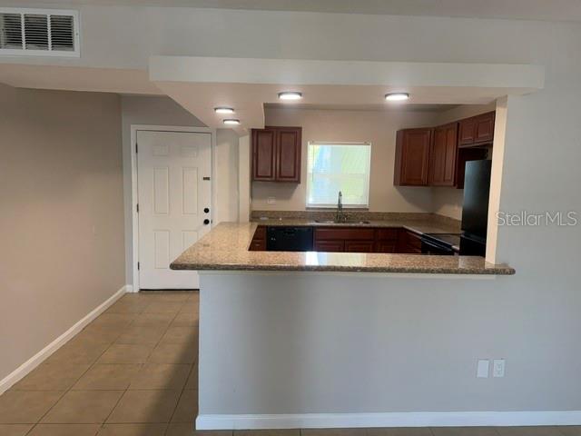 A kitchen with wood cabinets and a granite breakfast bar overlooks a tiled living area — 14413 AMERICANA CIRCLE UNIT 202, TAMPA, FL