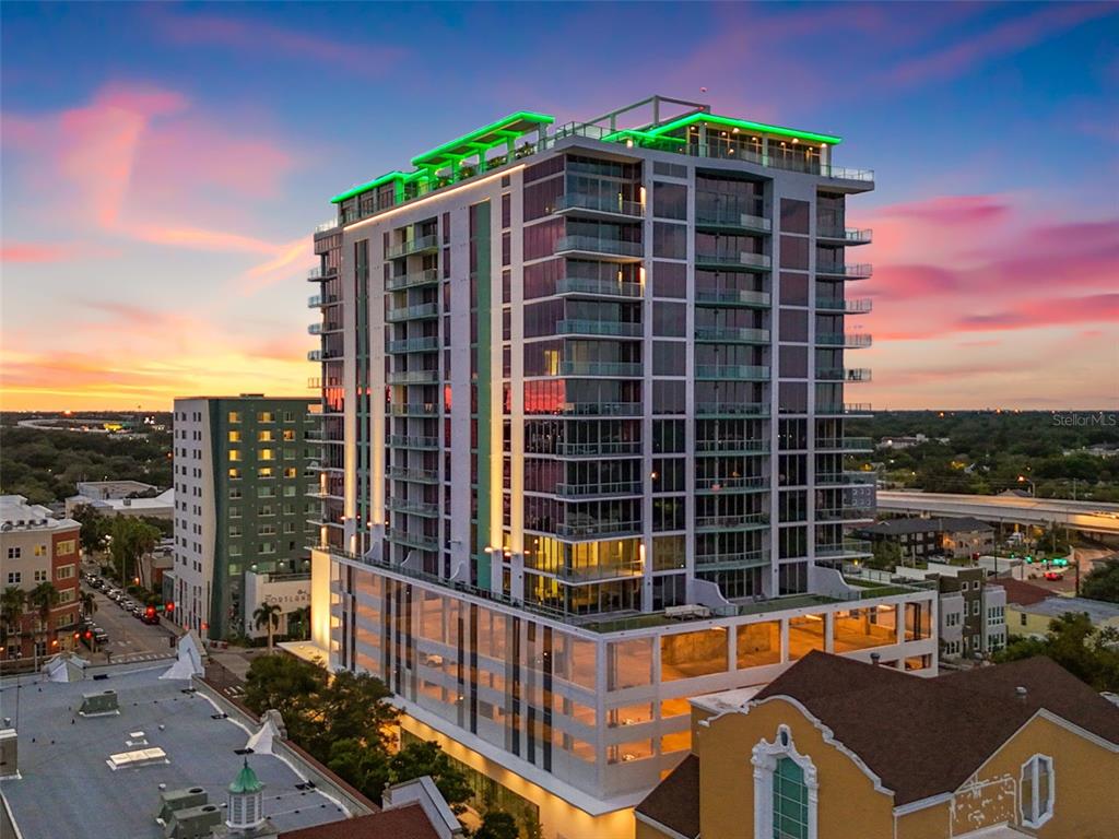 An aerial view of a modern high-rise apartment building with a green-lit rooftop at sunset — 777 3RD AVENUE N UNIT 805, ST PETERSBURG, FL
