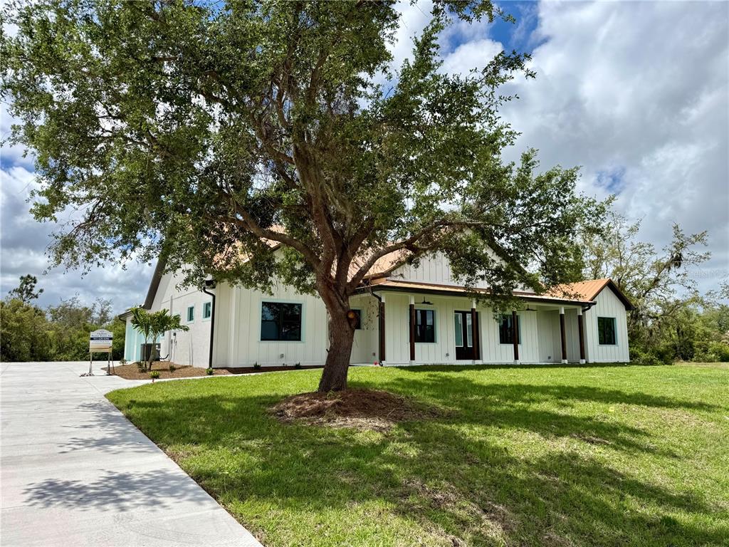 A white farmhouse-style home with a metal roof sits behind a large tree — 520 WOODSTORK LANE, PUNTA GORDA, FL