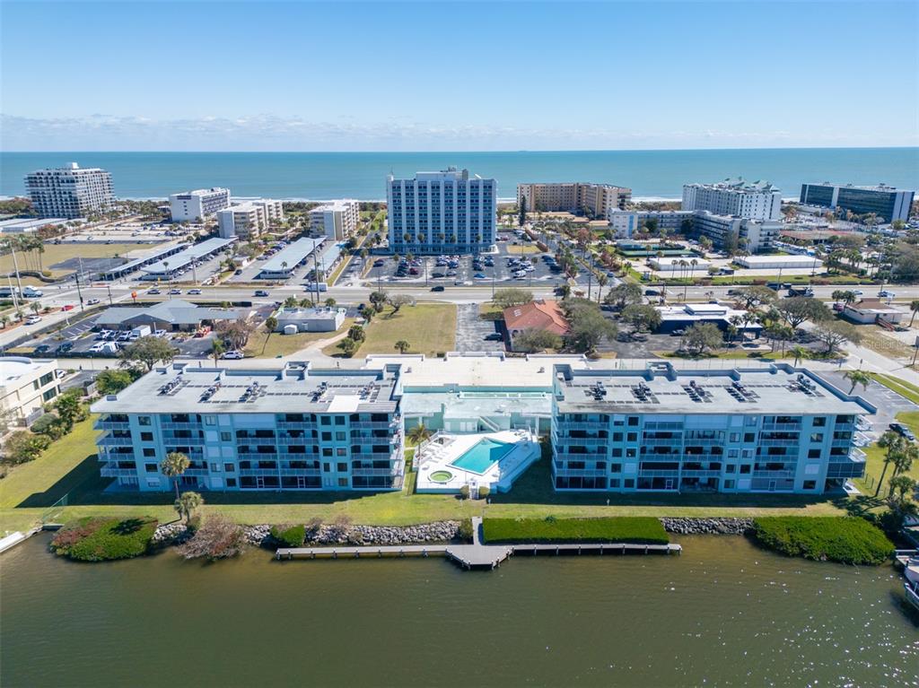 An aerial view shows a waterfront apartment complex with a pool and nearby beach buildings — 1750 COMMODORE BOULEVARD UNIT 2303, COCOA BEACH, FL